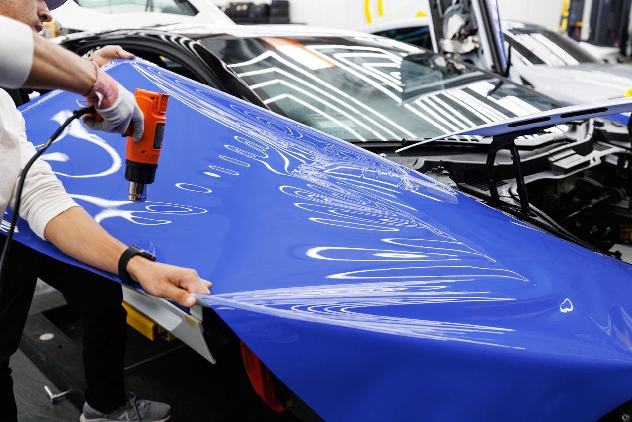 Services-03 A technician uses a heat gun to carefully apply a blue vinyl wrap to a car in an auto workshop.